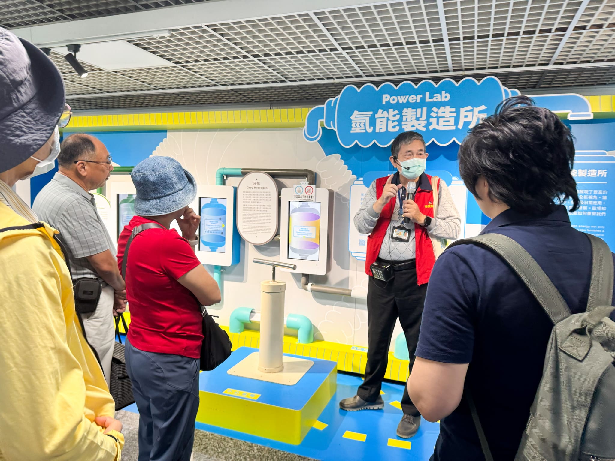 A museum guide explaining the Hydrogen Power Lab exhibit to JPE employees and their families, who are attentively listening.